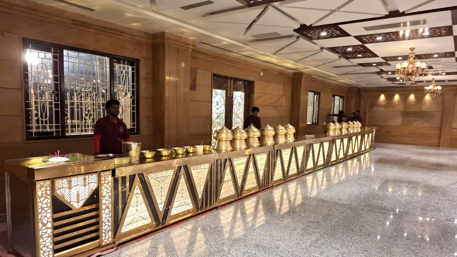 Long illuminated gold buffet counter lined with brass serving vessels at a Tirupati banquet hall